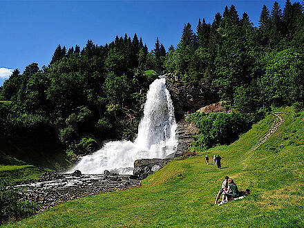 Urlauber sitzen auf der Wiese am Wasserfall Steindalsfossen in Norwegen