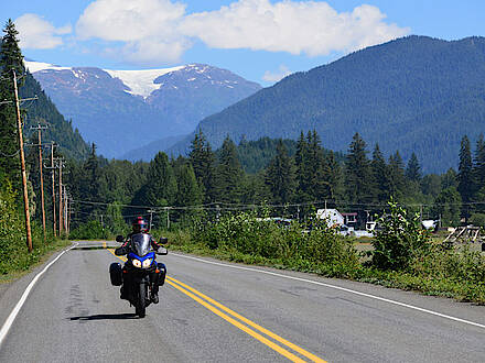 Motorrad fährt auf Highway mit Bergen im Hintergrund bei Stewart in Kanada