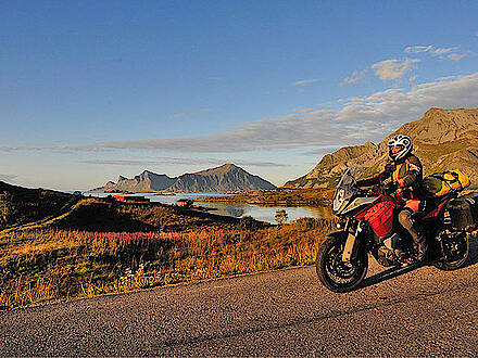 Motorrad auf einer Landstraße vor Bergen und dem Meer auf den Lofoten