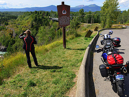 Motorradfahrerin blickt auf Bergkette und Hängebrücke bei Hazelton