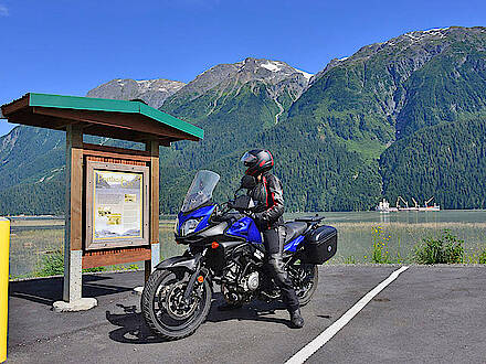 Motorradfahrerin blickt auf Karte am See mit Bergen im Hintergrund bei Hyder in Kanada