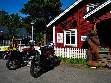KTM 1190 Adventure und Moto Guzzi Stevio vor einer roten Blockhütte in Finnland