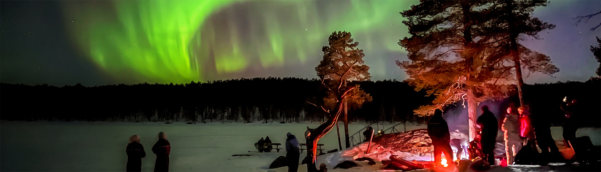 Menschen am Lagerfeuer beobachten Polarlichter im Winter in Lappland
