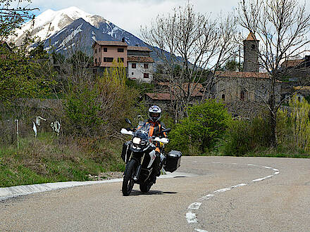 BMW F800 GS auf kurviger Landstraße vor einem Bergdorf und Gipfel in den Pyrenäen in Spanien