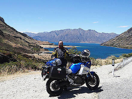Motorrad und Motorradfahrer vor einem See und Bergen in Neuseeland