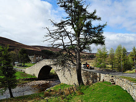 Motorrad auf alter Brücke mit Herrenhaus im Hintergrund in den Highlands in Schottland