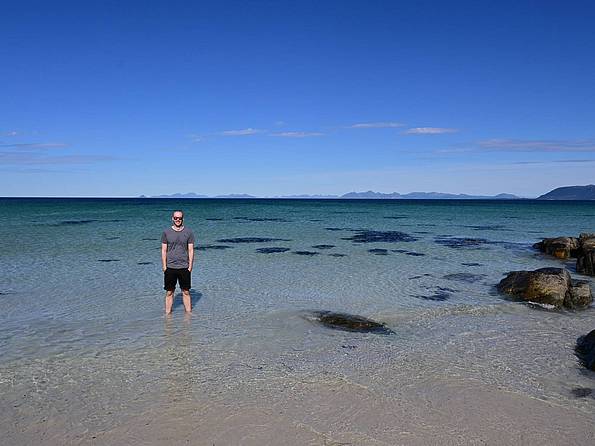 Ein Mann steht im Wasser am Strand auf den Lofoten