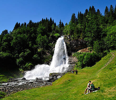Leute auf einer Wiese vor einem Wasserfall in Norwegen