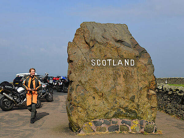 Motorräder und Motorradfahrerin an dem Grenzstein in Schottland