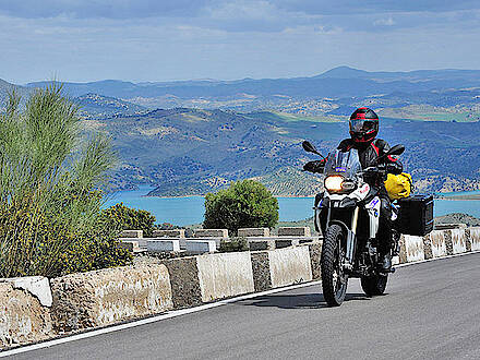 Motorrad auf kurviger Bergstraße vor Bergen und einem See in Andalusien
