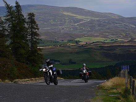 Motorräder auf einer Landstraße in den Highlands in Schottland vor grünen Hügeln