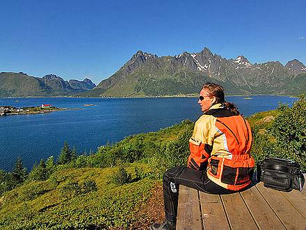Motorradfahrerin blickt über Meer und Berge auf den Lofoten in Norwegen