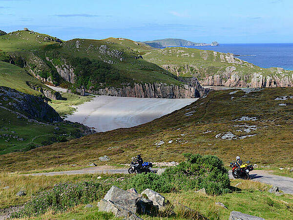 Motorräder auf Single Track vor einer Bucht mit Strand an der Nordwestküste von Schottland