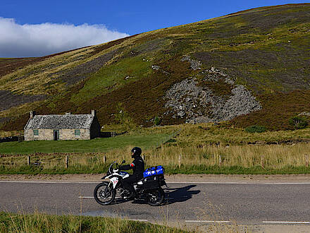 BMW F800 GS auf einer Landstraße vor einer alten Hütte in den Highlands in Schottland