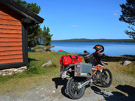 KTM Enduro vor rotem Holzhaus am See in Norwegen