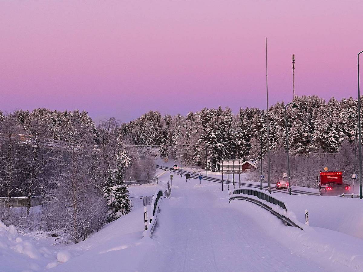 Rosa Winterlicht über einer verschneiten Straße im Norden Finnlands