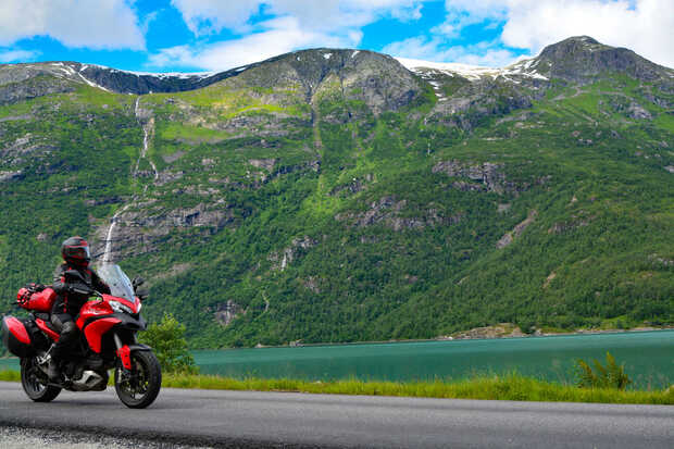 Ein Motorrad fährt in Norwegen an einem türkisen See entlang