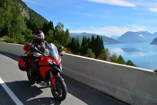 Ein rotes Motorrad fährt in Norwegen auf einer Landstraße