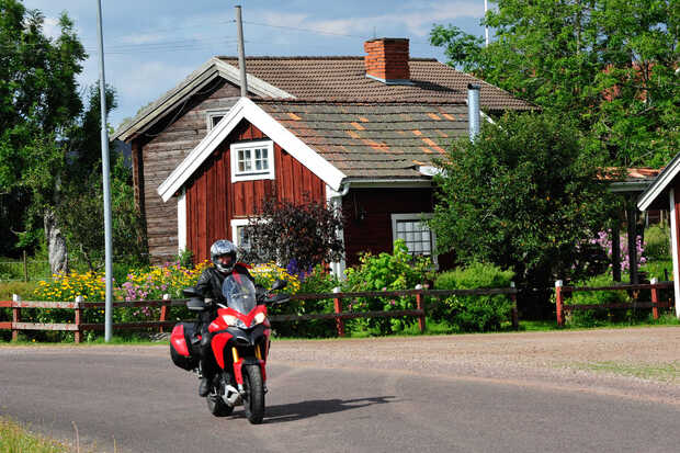 Eine rote Ducati fährt an roten Holzhäusern in Schweden vorbei